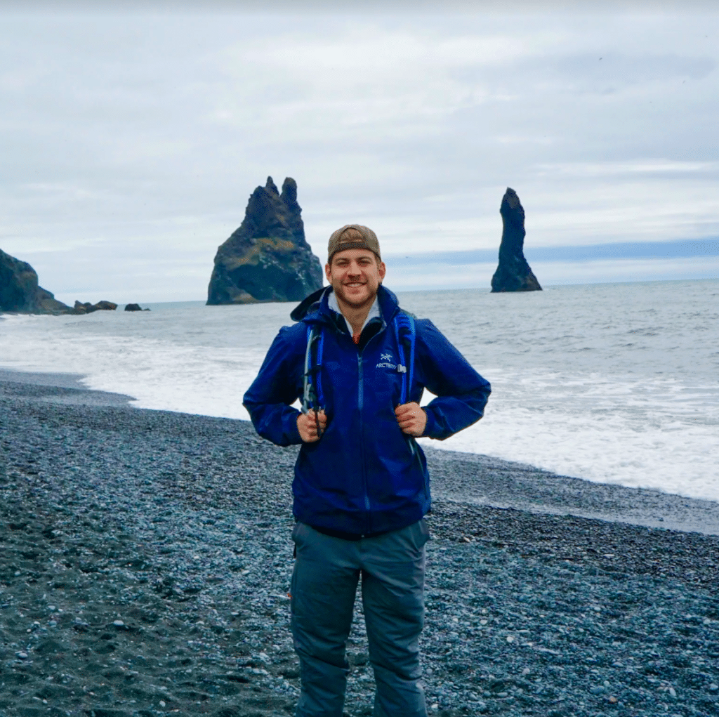 Paul Glushakov on black beach in front of rock formation in the arctic