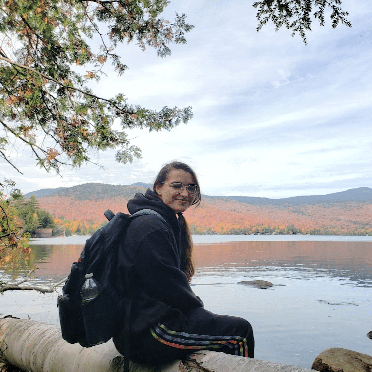 Audrey Reyes hiking sitting near lake on log with backpack