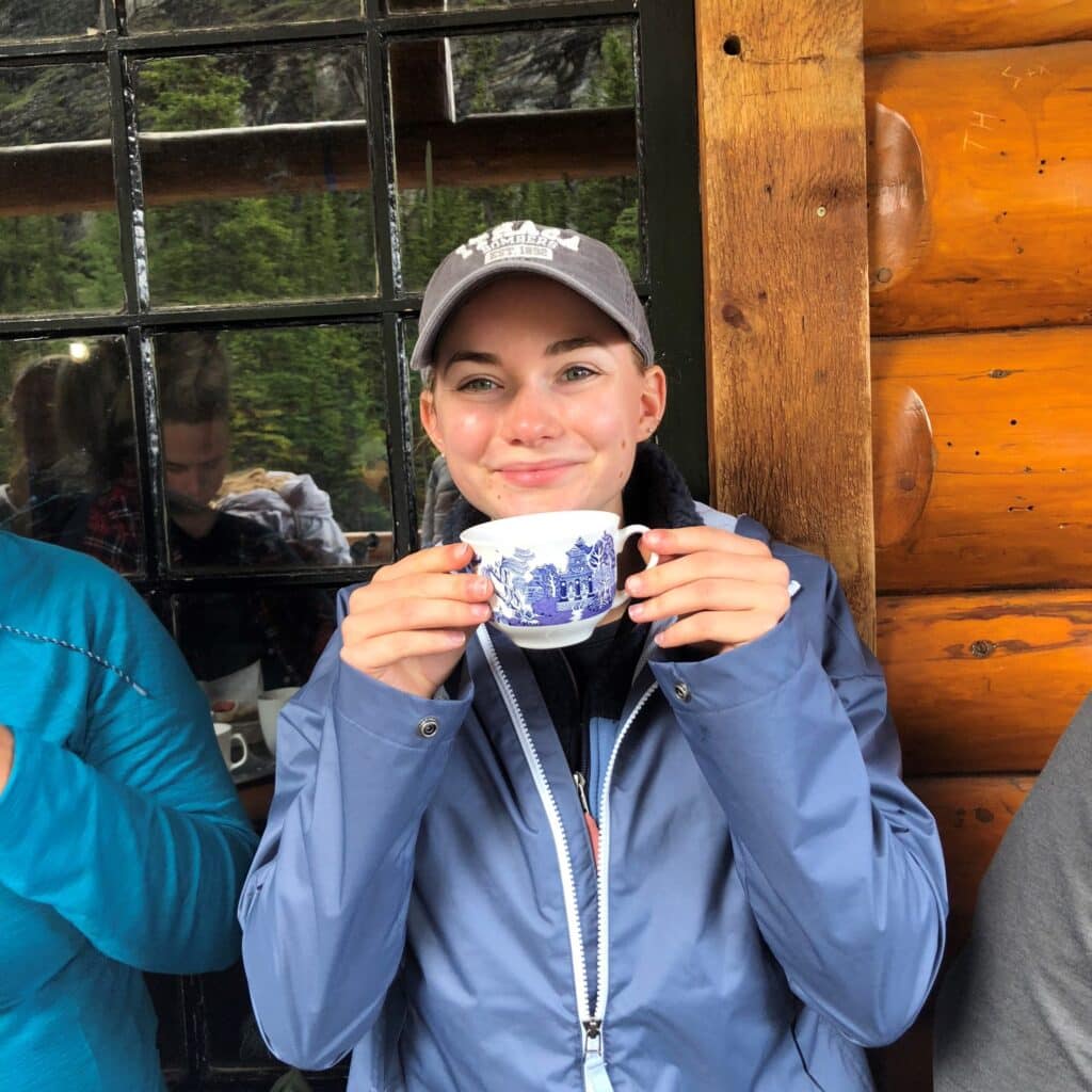 Jennie Brian drinking out of a cup in front of a hut