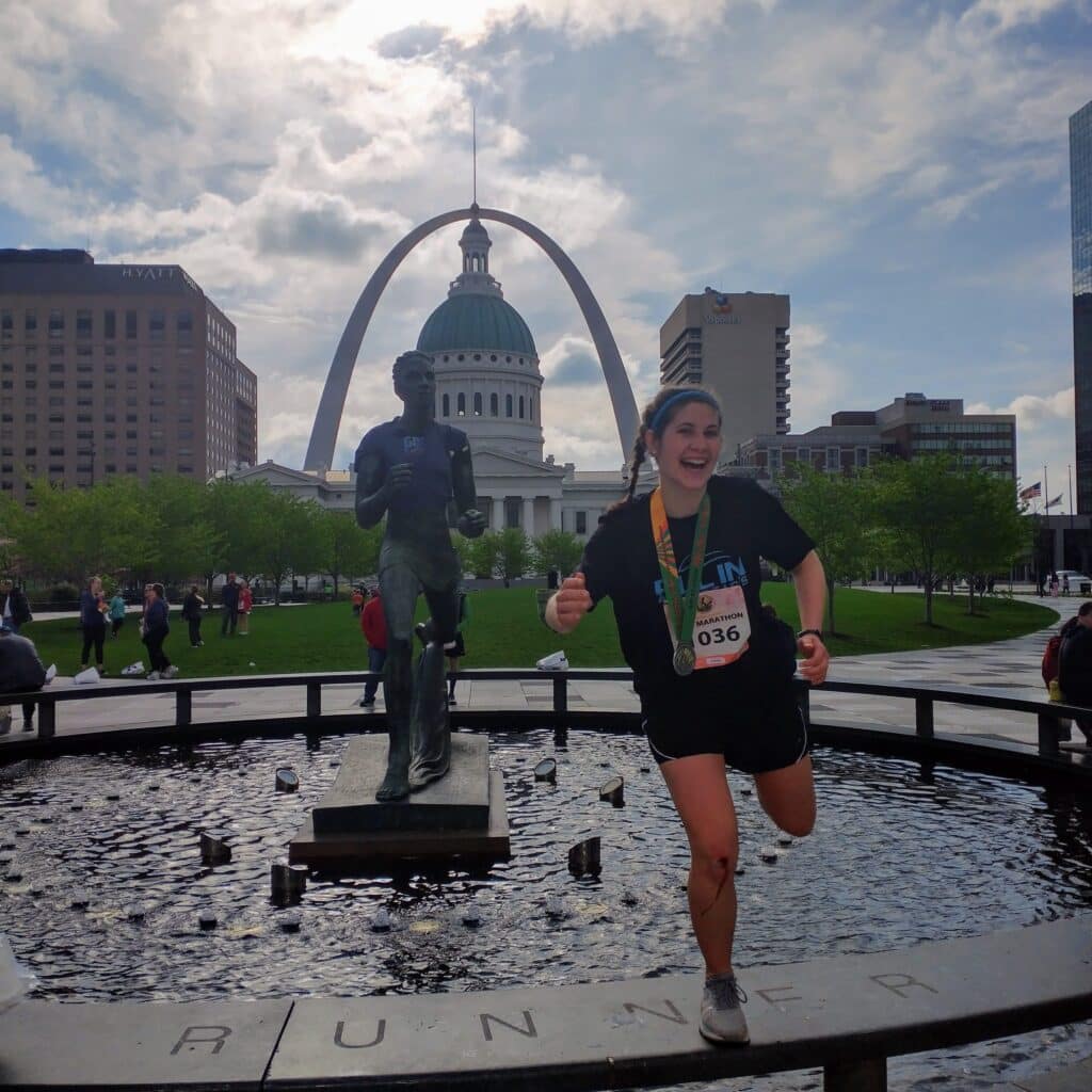 Mandy Mongoven in running apparel posing in front of running statue with medal