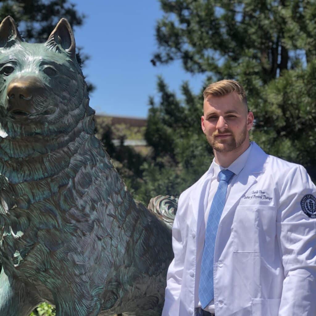 Jake Ober taking a graduation photo next to a ststue of the school mascot